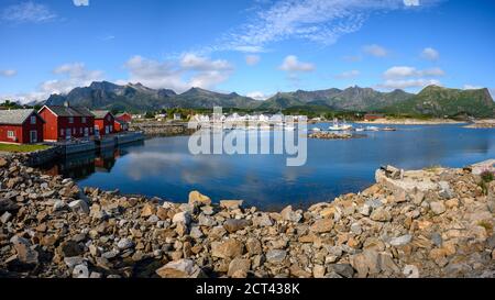 Panoramablick, Rote Hütte mit blauem Himmel, der das Wasser am Kabelvaag auf den Lofoten-Inseln im Norden Norwegens reflektiert. Stockfoto