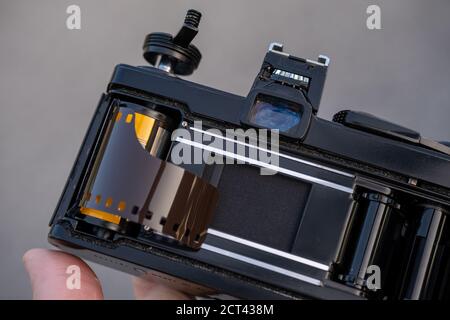 Eine Hand hält eine alte analoge Spiegelreflexkamera mit geöffneter Rückseite, wobei eine Rolle 35-mm-Farb-Negativfilm in die Spule gelegt wird, die geladen werden kann. Stockfoto