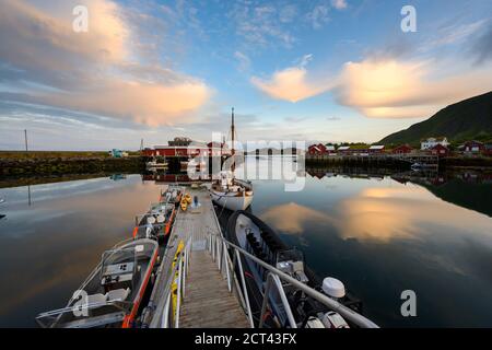 Fischerboot und rotes Dorf, das am Abend das Wasser reflektiert in Ballstad, Nordnorwegen, ist Rorbu die traditionelle Heimat der norwegischen Fischer. Stockfoto
