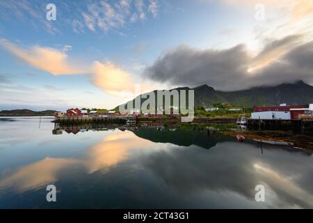 Fischerboot und rotes Dorf, das am Abend das Wasser reflektiert in Ballstad, Nordnorwegen, ist Rorbu die traditionelle Heimat der norwegischen Fischer. Stockfoto
