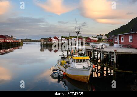 Fischerboot und rotes Dorf, das am Abend das Wasser reflektiert in Ballstad, Nordnorwegen, ist Rorbu die traditionelle Heimat der norwegischen Fischer. Stockfoto