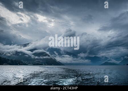 Landschaft des dunklen Comer Sees mit sehr bewölktem Himmel und Bergen, die in Norditalien liegt. Stockfoto