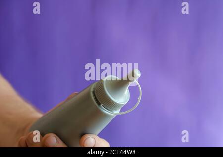 Männliche Hand und graue Plastikflasche mit Sirup. Der Mann hält eine neue Flasche Süßsirup für Eis und Desserts. Selektiver Fokus. Stockfoto
