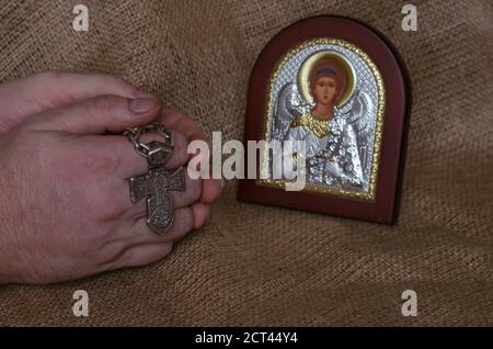 Hände gefaltet im Gebet mit einem silbernen Kreuz vor der Ikone des Erzengels Michael. Christlich-orthodoxe Ikone. Ein Moment des Gebets. Stockfoto