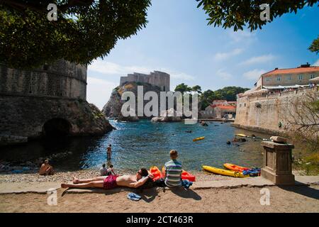 Menschen entspannen am Strand von Dubrovnik, gegenüber Fort Lovrijenac, Dubrovnic, Kroatien Stockfoto