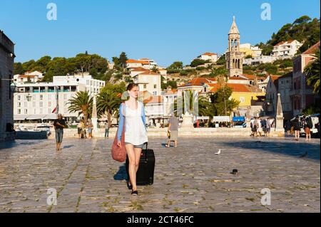 Tourist Frau Reisen, gehen in den Sommerurlaub, Ankunft mit Koffer und zu Fuß durch Hvar Stadt, Insel Hvar, Kroatien Stockfoto