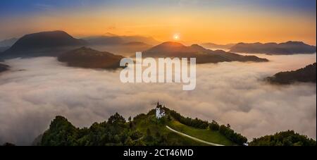 Sebrelje, Slowenien - Luftpanorama Drohne Blick auf die schöne Hügelkirche St. Ivan (Sv. Ivan Cerkev) bei Sonnenaufgang mit riesigem Morgennebel Stockfoto