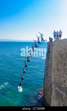 Acre, Israel - 14. September 2020: Junger Araber springt von der alten Stadtmauer zum Meer, während andere in Akko, Israel, zuschauen. Mehrfacher Hirsch Stockfoto