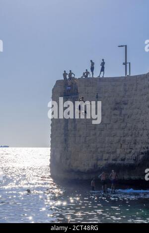 Acre, Israel - 14. September 2020: Junger Araber springt von der alten Stadtmauer zum Meer, während andere in Akko, Israel, zuschauen Stockfoto