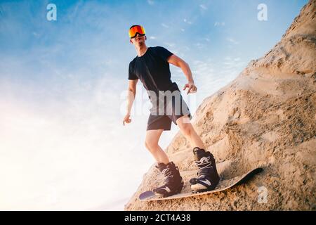 Extremer Absand auf Snowboard in der Wüste. Männlicher Snowboarder auf Dünen Stockfoto