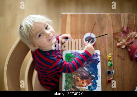 Süßes Kleinkind Junge mit roter Schürze, Malerei zu Hause mit Wasser Farben Stockfoto
