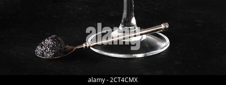 Schwarzes Kaviar-Panorama, ein silberner Löffel mit einem Glas Champagner auf schwarzem Hintergrund Stockfoto