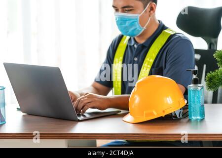 Quarantäne, Close-up-Helm asiatischen Ingenieur trägt Gesicht schützende medizinische Maske zum Schutz vor Viruserkrankungen mit Laptop-Computer im Bau Stockfoto