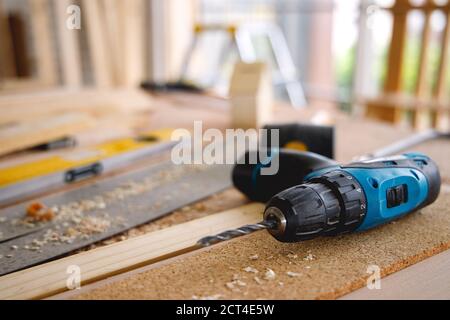 Blaue elektrische Bohrmaschine, auf dem Holztisch voller Sägemehl, mit für Holzarbeiten oder Reparatur Hause innen. Stockfoto