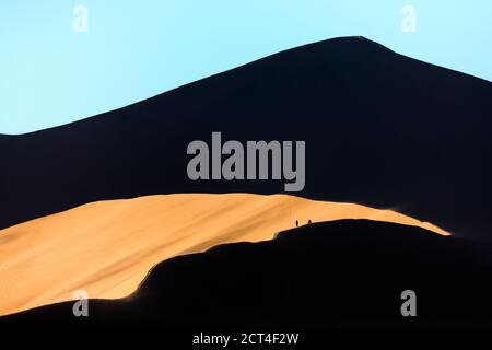 Touristen steigen im Morgenlicht in Sossusvlei, Namibia, auf eine große rote Sanddüne. Stockfoto