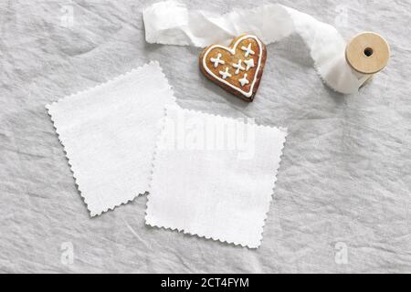 Weihnachten Textil Mockup Szene. Weiße Baumwollstoffe Muster auf Leinen Tischtuch Hintergrund. Lebkuchen Herzkekse, dekorative Zuckerguss und Stockfoto