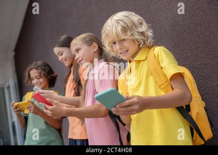 Vier Kinder stehen nebeneinander mit Smartphones Hände und spielen online Stockfoto