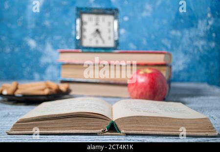 Ein offenes Buch auf dem Hintergrund eines Stapels von Bücher und ein Apfel mit einer Uhr Stockfoto