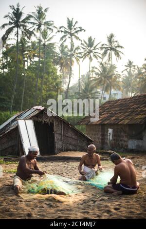 Fischer flicken Fischernetze unter tropischen Palmen bei Sonnenaufgang am Kappil Beach, Varkala, Kerala, Indien Stockfoto