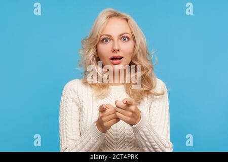 Nahaufnahme aufgeregt wunderte Frau mit blonden lockigen Haaren zeigt Finger auf Sie, schockiert und überrascht, Erstaunen. Innenaufnahme des Studios isoliert auf Blau Stockfoto