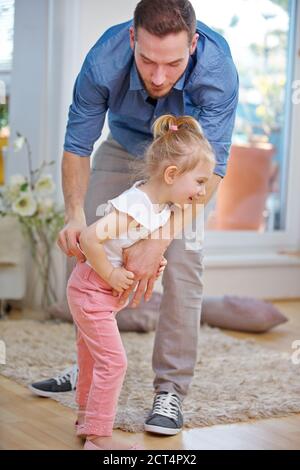 Vater hilft seiner Tochter, sich zu Hause Hosen an zu ziehen Stockfoto