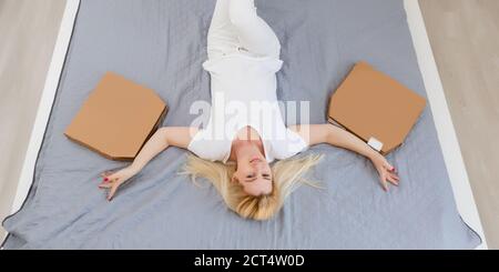 Junge Frau, die auf einem Sofa liegt und Pizza isst Stockfoto