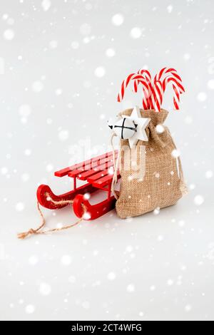 Roter Schlitten und Zuckerrüben im Jutesack mit Weihnachtsdekoration und Schneeflocken. Stockfoto