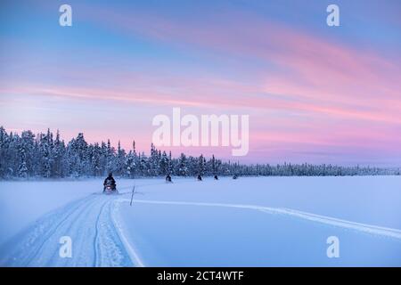 Motorschlittenfahrt auf dem gefrorenen See bei Sonnenuntergang in Torassieppi, Lappland, Finnland Stockfoto