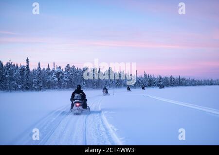 Motorschlittenfahrt auf dem gefrorenen See bei Sonnenuntergang in Torassieppi, Lappland, Finnland Stockfoto