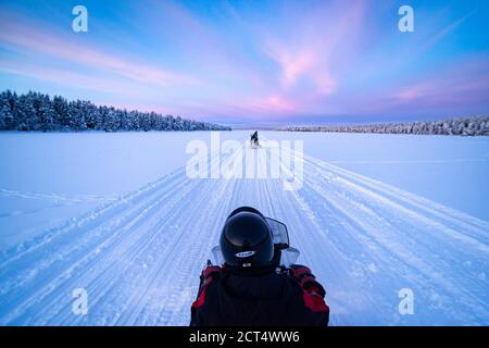 Motorschlittenfahrt auf dem gefrorenen See bei Sonnenuntergang in Torassieppi, Lappland, Finnland Stockfoto