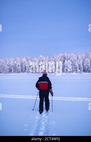 Ein Mann, der bei Sonnenuntergang auf dem gefrorenen See von Torassieppi Ski fährt und die Einsamkeit einer abgelegenen einsamen Landschaft, Lappland, Finnland, erlebt Stockfoto