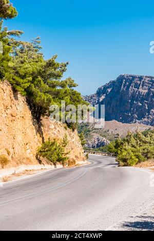 Asphaltstraße in den Bergen der Insel Karpathos, mit einer weißen Kapelle auf der Spitze in der Ferne, Griechenland Stockfoto