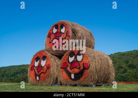 Drei gerollte Heufässer, die in einer Pyramide gestapelt werden Form mit bemalten Cartoon Gesichter sind in der Mitte gefunden Von einem Feld an einem sonnigen Tag ohne Clou Stockfoto