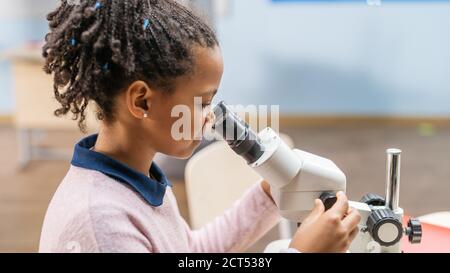 Portrait von Smart Little Schoolgirl Blick unter dem Mikroskop. In Grundschule Klassenzimmer Cute Girl Nutzt Mikroskop. MINT-Wissenschaft, Technologie Stockfoto