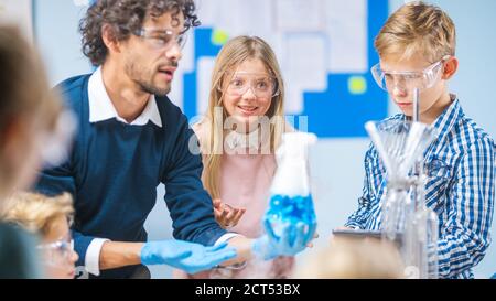 Grundschule Wissenschaft Klassenzimmer: Begeisterter Lehrer erklärt Chemie zu verschiedenen Gruppe von Kindern, zeigt ihnen, wie man Chemikalien in Bechern mischen Stockfoto