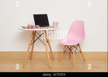 Ein Laptop und Rosen sind auf dem Tisch, neben einem rosa Stuhl. Stockfoto