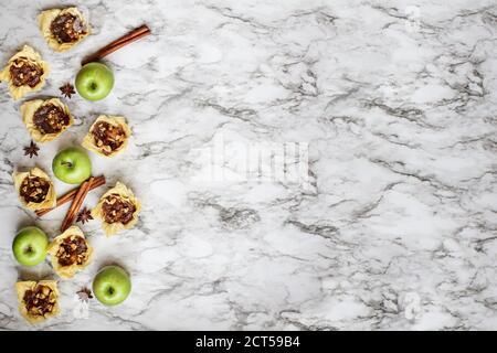 Mini-Apfelkuchen mit Phyllo-Kruste mit frischen Früchten, Anisstern und Zimtrinde auf weißem und schwarzem Marmorboden. Draufsicht oder Flatlay. Stockfoto