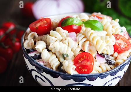 Nudelsalat mit Rotini-Nudeln, frisch gehacktem Basilikum, Kirschtomaten, schwarzen Oliven, roten Zwiebeln und Feta-Käse, mit einem italienischen Öldressing gewürzt. Stockfoto