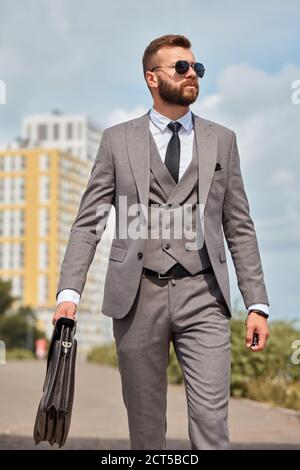Porträt eines gutaussehenden kaukasischen Geschäftsmannes mit Tasche, die bei einer Geschäftssitzung in formellen Anzug im Freien geht Stockfoto