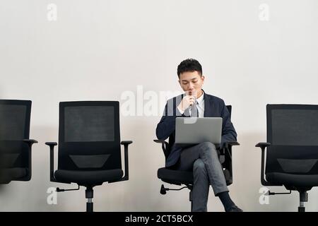 Junge asiatische Arbeitssuchende sitzen im Stuhl Vorbereitung für Interview Mit Laptop-Computer während der Wartezeit in der Schlange Stockfoto