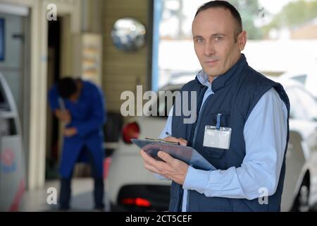 Selbstbewusster Geschäftsmann hält Zwischenablage gegen Werkstatt Stockfoto