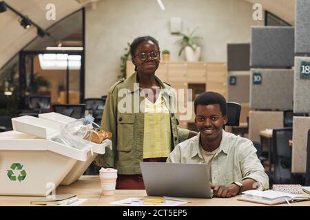 Porträt lächelnder afroamerikanischer Menschen, die in die Kamera schauen, während sie an Müllsortierkörben im modernen Büro posieren, Kopierraum Stockfoto