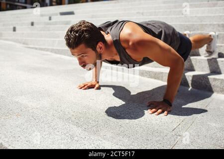 Junger Mann, der draußen trainiert. Hart arbeitend Athlet tun Push-up-Übung allein an den Stufen außerhalb. Mann trainiert und arbeitet an seiner Körperform. Immer Stockfoto