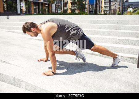 Junger Mann, der draußen trainiert. Athletist macht Bergsteiger Training. Ausübung allein in horizontaler Position am städtischen Gebäude. Stark leistungsstark Stockfoto
