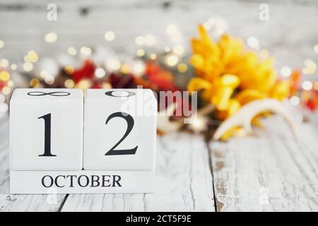 Weiße Holz-Kalenderblöcke mit dem Datum 12. Oktober und Herbstdekorationen über einem Holztisch. Selektiver Fokus mit unscharfem Hintergrund. Nationale Fa Stockfoto