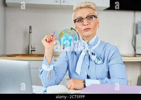 Porträt von selbstbewussten gut aussehenden Lehrer am Tisch sitzen, junge kurzhaarige Frau in formeller Kleidung halten Online-Bildung mit Laptop Stockfoto