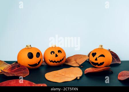 Kleine Kürbisse mit bemalten Gesichtern für Halloween mit Herbstblättern Auf blauem und schwarzem Hintergrund Stockfoto