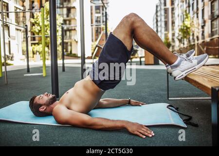 Junger Mann, der draußen trainiert. Gut gebaut muskulösen Kerl stehen in umgekehrter Plank Position mit Beinen nach oben. Hände am Boden halten und trainieren. Allein bei Stockfoto