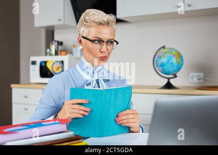 Ärgerlicher unzufriedener Lehrer betrachten Laptop zu Hause, halten Buch in den Händen, müde des Hörens auf den Unsinn der Schüler Stockfoto
