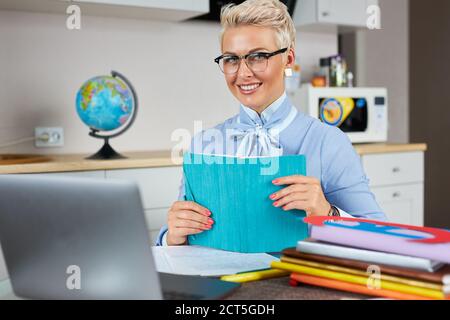 Blonde kaukasische weibliche junge Schullehrerin mit Webcam zu Hause, virtuelles Unterrichtskonzept, geben Remote-Klasse Online-Unterricht per Zoom Konferenzgespräch Stockfoto
